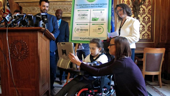 Norah Lowe, 10, speaks through a computer in favor of legalizing medical marijuana with her mother, Megan, at her side while her dad, Josh, stands at the podium and state Rep. Melissa Sargent watches on Thursday, April 18, 2019, in Madison, Wisc. The Lowes and others attended a news conference announcing Sargent's latest attempt in the Wisconsin Legislature to legalize marijuana.