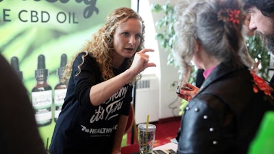 In this April 7, 2019 photo, Lindsey Bouras, left, wellness consultant at The Healthy Place, formerly known as Apple Wellness, talks to an attendee about CBD oil at the, It's Hemp, It's Fine hemp/CBD event, at Monona Terrace Convention Center in Madison, Wisc. The event featured a panel discussion, informational booths, and free samples of CBD coffee, beer, kombucha, candy and more.