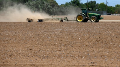 In this May 23, 2018, file photo, a farmer plows a dry and dusty cotton field in Phoenix.
