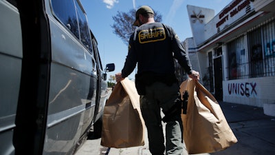 In this March 15, 2018, file photo, a Los Angeles County sheriff's deputy loads two evidence bags into a van after raiding an illegal marijuana dispensary in Compton, Calif.