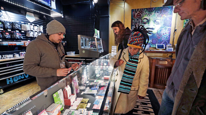 In this Jan. 4, 2018, file photo, cannabis consultant Juan Aguilar, left, assists customers in the Herban Legends pot shop in Seattle.