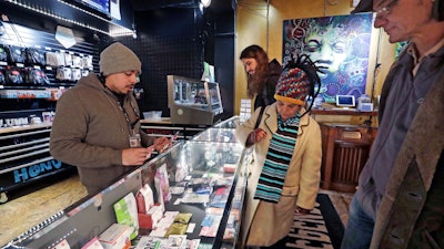 In this Jan. 4, 2018, file photo, cannabis consultant Juan Aguilar, left, assists customers in the Herban Legends pot shop in Seattle.