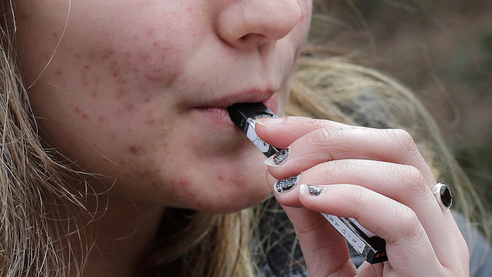 In this April 11, 2018, file photo, a high school student uses a vaping device near a school campus in Cambridge, Mass.