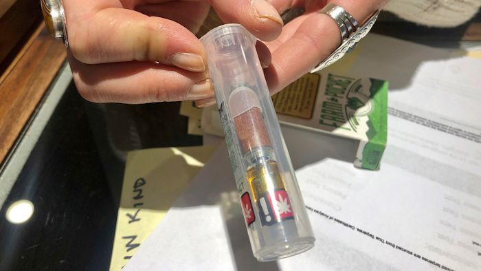 In this photo taken Sept. 20, 2019, Cameron Moore, general manager of Bridge City Collective in Portland, Ore., holds a vape cartridge that's on sale at the dispensary. The company had a 31% drop in sales of vape cartridges that hold the oil that vaporizes when heated. Vaping products are taking a hit as health experts scramble to determine what’s causing a mysterious lung disease.