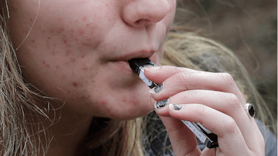 In this April 11, 2018, file photo, a high school student uses a vaping device near a school campus in Cambridge, Mass.