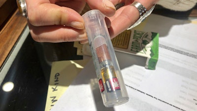 In this photo taken Sept. 20, 2019, Cameron Moore, general manager of Bridge City Collective in Portland, Ore., holds a vape cartridge that's on sale at the dispensary. The company had a 31% drop in sales of vape cartridges that hold the oil that vaporizes when heated. Vaping products are taking a hit as health experts scramble to determine what’s causing a mysterious lung disease.