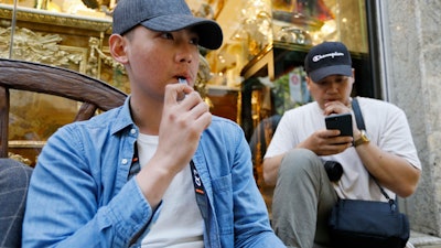 In this Monday, June 17, 2019, photo, Joshua Ni, 24, and Fritz Ramirez, 23, vape from electronic cigarettes in San Francisco.
