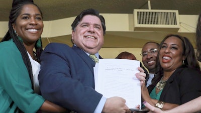 In this June 25, 2019 file photo, Gov. J. B. Pritzker holds a bill that legalizes adult-use cannabis in the state of Illinois accompanied by state Rep. Kelly Cassidy, left, and state Sen. Toi Hutchinson, right, in Chicago. Illinois becomes the 11th to legalize the adult-use of recreational marijuana. Like in other states before it, advocates of legalizing recreational marijuana use in Illinois want the law to look backward as well as forward. It conscientiously attempts to ensure that those who profit from growing and selling the weed have substantial representation from the mostly impoverished neighborhoods nailed the hardest by decades of drug crackdowns.