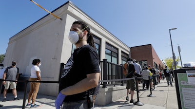 A staff member at Pure Oasis recreational marijuana store walks past a line of customers, May 26, 2020, Boston.