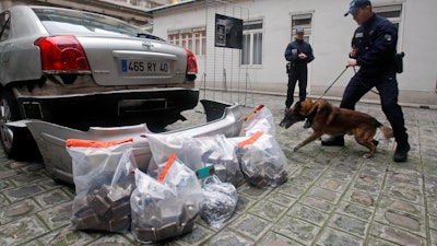 In this Jan. 15, 2020, file photo, police officers and a police sniffer dog stand next to 63 kilos of marijuana which where found in the car seen left, during a press conference in Paris. France's government launched a two-year nationwide experiment with medical cannabis with a view to eventual legalization.