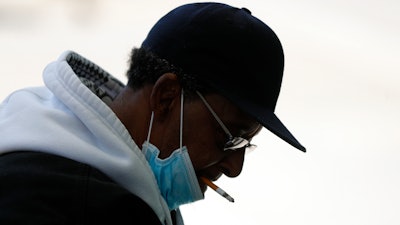 A man with a protective mask smokes a cigarette while waiting for a bus in Detroit, April 8, 2020.