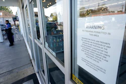 A sign warns that firearms are prohibited at Mary Mart, a marijuana store, Tuesday, April 19, 2022, in Tacoma, Wash., as armed security guard Austin MacMath stands watch outside at left. A surge in robberies at licensed cannabis shops in Washington state is helping fuel a renewed push for federal banking reforms that would make the cash-dependent stores a less appealing target.