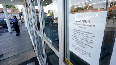 A sign warns that firearms are prohibited at Mary Mart, a marijuana store, Tuesday, April 19, 2022, in Tacoma, Wash., as armed security guard Austin MacMath stands watch outside at left. A surge in robberies at licensed cannabis shops in Washington state is helping fuel a renewed push for federal banking reforms that would make the cash-dependent stores a less appealing target.