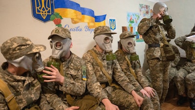Cadets practice putting on gas masks during a lesson in a bomb shelter in a cadet lyceum in Kyiv, Ukraine, Tuesday, June 6, 2023. Writing on the wall reads: 'Glory to Ukraine.'