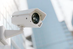 White security camera mounted on exterior wall with urban building in background