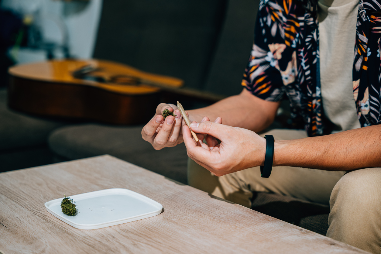 Two people examining a small cannabis bud on a wooden table during an indoor social gathering