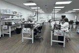 Modern laboratory workspace with multiple workstations, white cabinetry, LED lighting, and staff conducting research or analysis