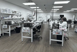 Modern laboratory workspace with multiple workstations, white cabinetry, LED lighting, and staff conducting research or analysis