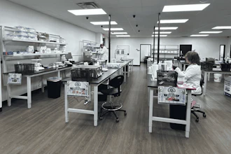 Modern laboratory workspace with multiple workstations, white cabinetry, LED lighting, and staff conducting research or analysis