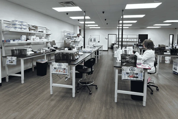 Modern laboratory workspace with multiple workstations, white cabinetry, LED lighting, and staff conducting research or analysis