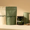 CropPak sustainable packaging collection featuring cream and green pouches, black glass jar, and cardboard tube on neutral background
