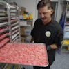 Worker holding tray of pink gummy candies in commercial kitchen with shelving and inventory