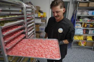 Worker holding tray of pink gummy candies in commercial kitchen with shelving and inventory