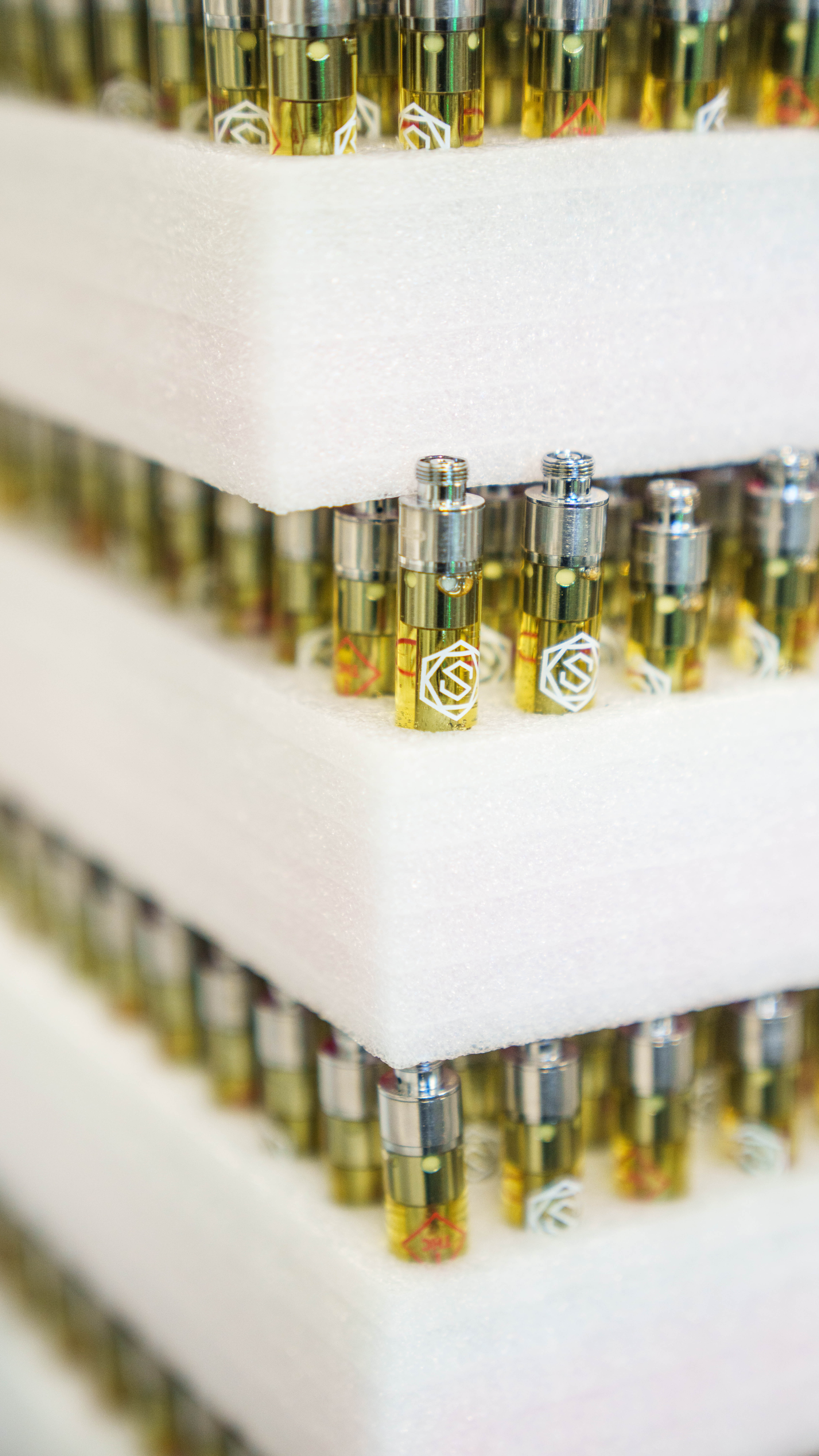 Tiered display of yellow-tinted fragrance bottles with metallic caps and white emblems arranged on white shelving