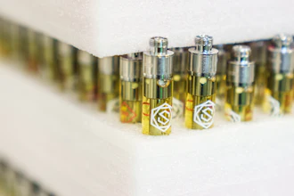 Tiered display of yellow-tinted fragrance bottles with metallic caps and white emblems arranged on white shelving