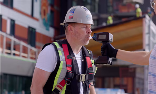 Construction worker wearing safety helmet and reflective vest holding surveying equipment on active job site