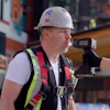 Construction worker wearing safety helmet and reflective vest holding surveying equipment on active job site