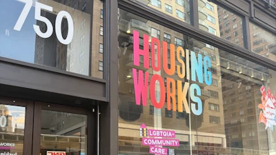 Housing Works storefront at 750 with pink signage, LGBTQIA+ community care messaging, and cannabis dispensary window display on urban street