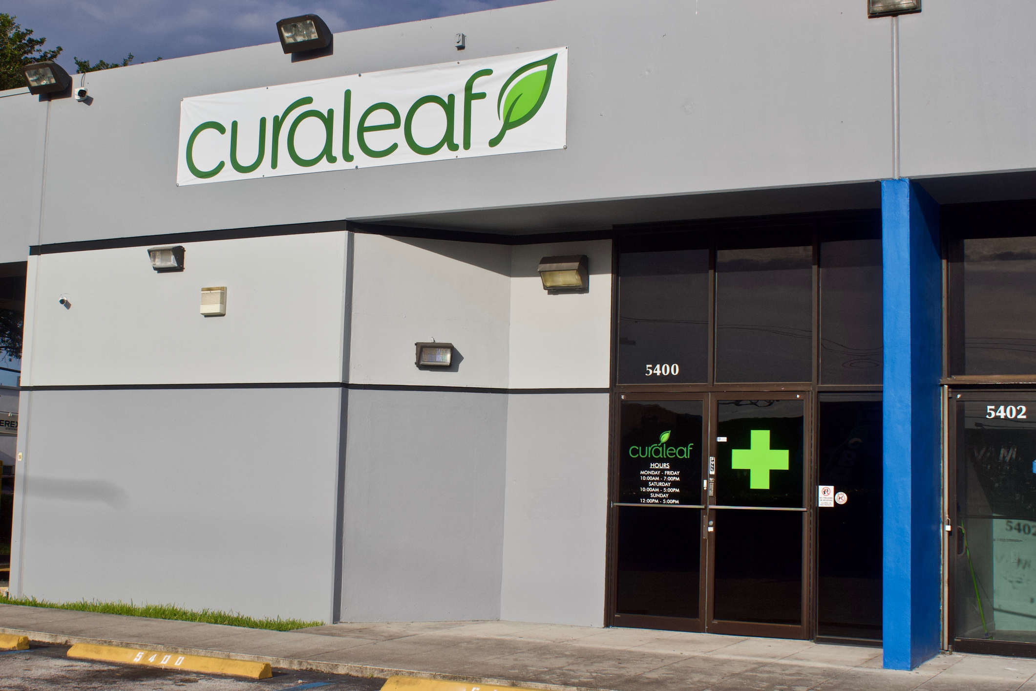 Curaleaf dispensary storefront with green logo, blue pillar, and dark entrance doors at address 5400