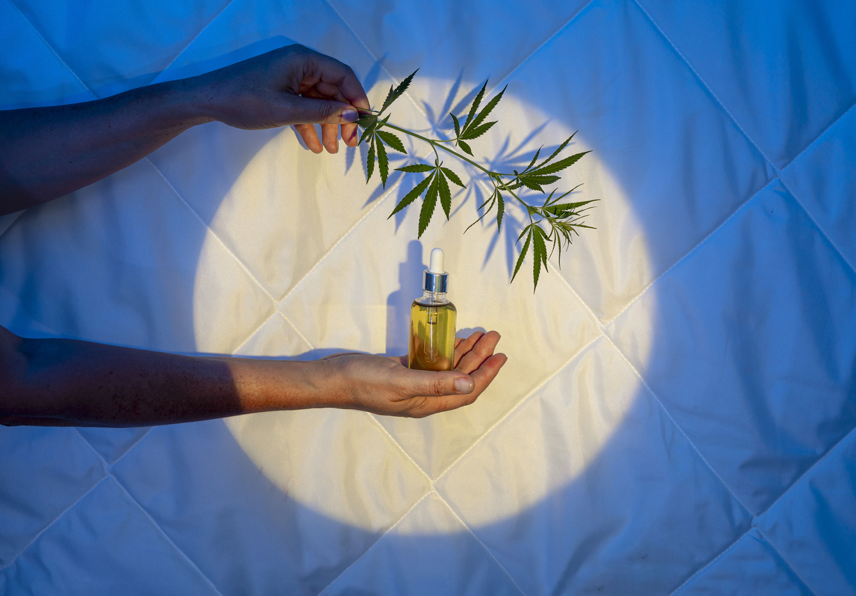 Hand holding golden oil bottle with cannabis leaf branch against glowing circular backdrop