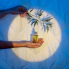 Hand holding golden oil bottle with cannabis leaf branch against glowing circular backdrop