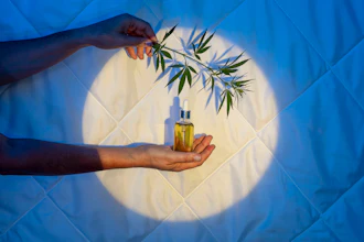 Hand holding golden oil bottle with cannabis leaf branch against glowing circular backdrop