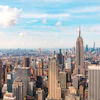 New York City skyline featuring the Empire State Building with surrounding skyscrapers under a blue sky with white clouds
