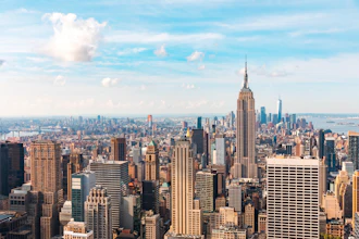 New York City skyline featuring the Empire State Building with surrounding skyscrapers under a blue sky with white clouds