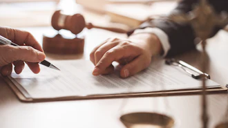 Two professionals reviewing and signing a legal document at a desk with a rubber stamp nearby