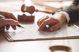 Two professionals reviewing and signing a legal document at a desk with a rubber stamp nearby
