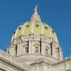 Pennsylvania State Capitol building with distinctive golden dome and classical architecture against clear blue sky