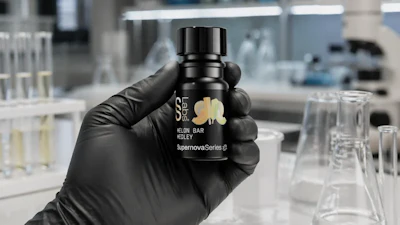 Black cosmetic bottle with gold leaf logo held in gloved hand in laboratory setting