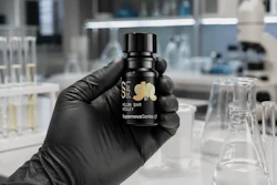 Black cosmetic bottle with gold leaf logo held in gloved hand in laboratory setting