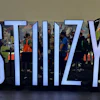 Large blue STIIIZY text installation at indoor event with attendees and branded merchandise displays