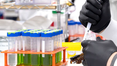 Scientist in black gloves holding labeled test tube in laboratory with colorful sample containers in orange rack