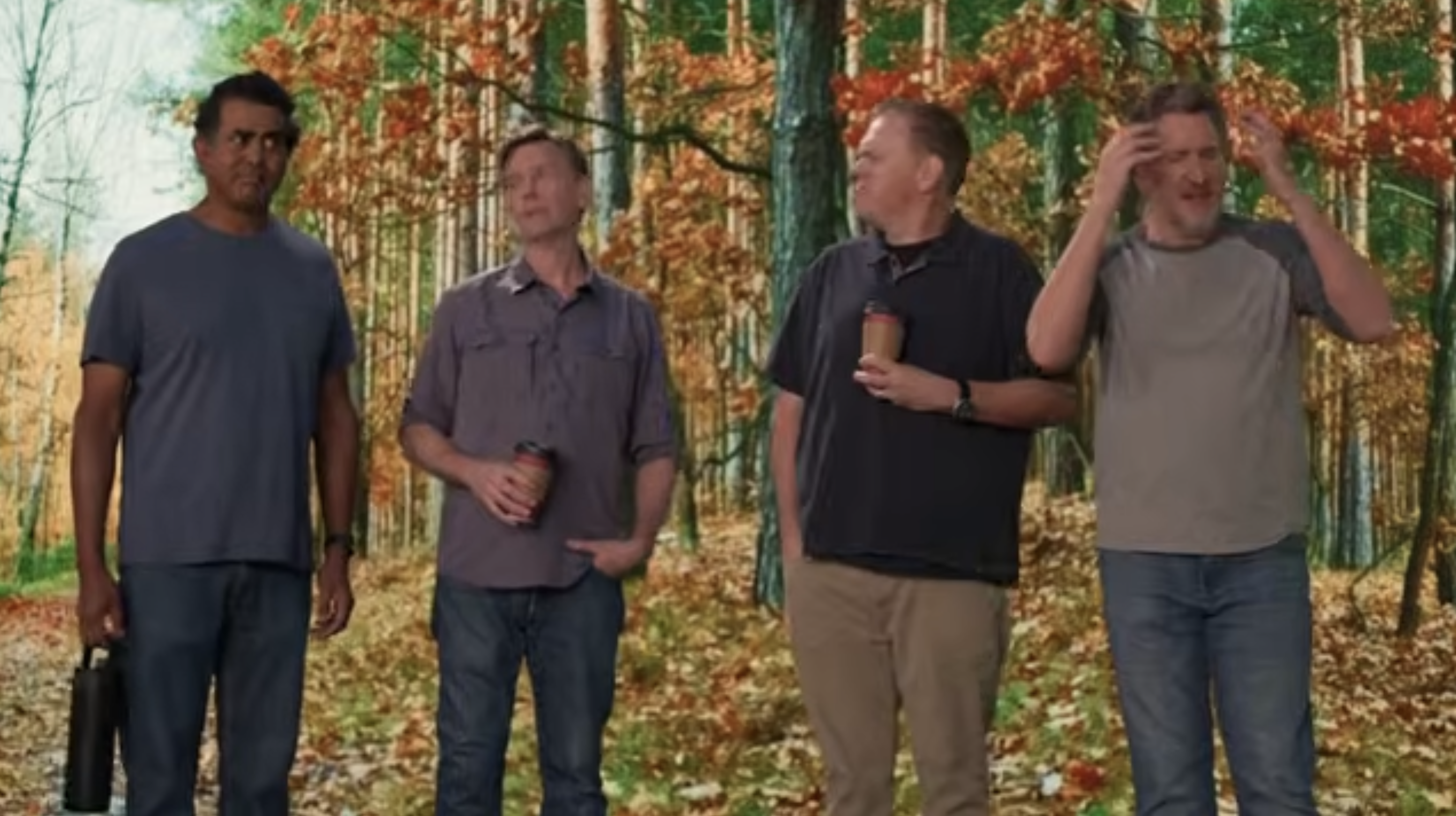 Four men stand together in an autumn forest with golden foliage in the background