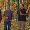 Four men stand together in an autumn forest with golden foliage in the background
