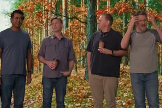 Four men stand together in an autumn forest with golden foliage in the background